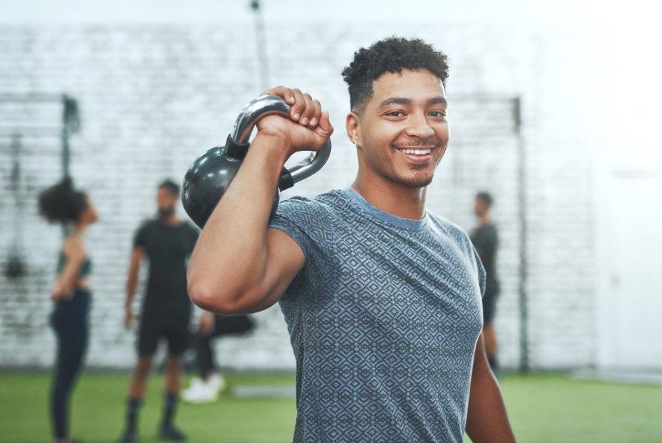 Person performing kettlebell shoulder exercise in a gym with other individuals in the background.