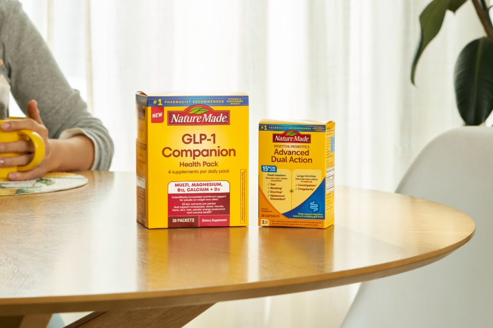 Nature Made GLP-1 Companion Health Pack and Advanced Dual Action supplements on a wooden table next to a yellow mug