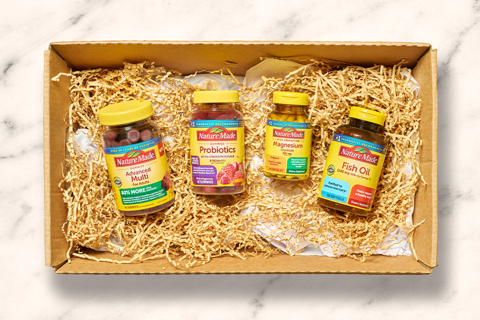 Nature Made vitamins and supplements in a gift box with shredded paper, featuring Advanced Multi, Probiotics, Magnesium, and Fish Oil bottles.