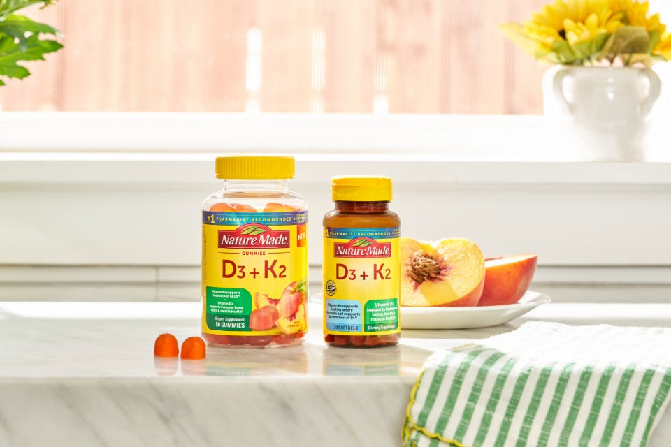 Nature Made D3 + K2 supplements in gummy and softgel form on a marble counter with peach slices.
