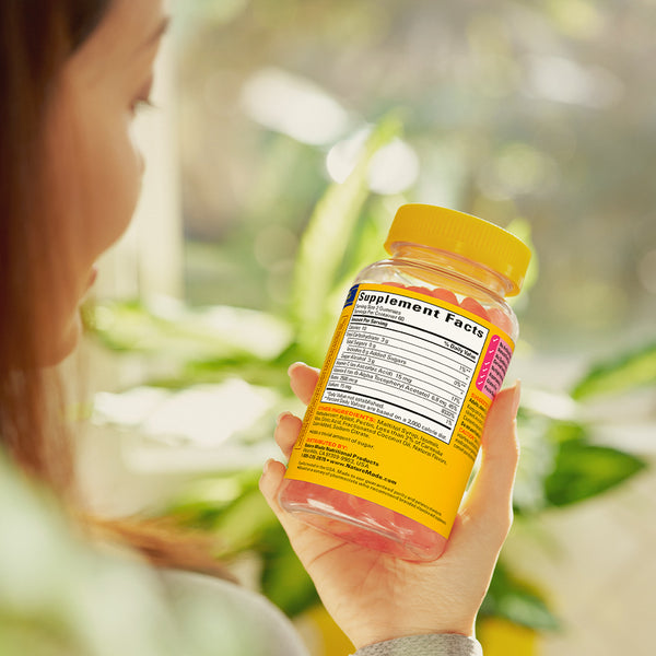 A person reading the supplement facts label of a Nature Made Zero Sugar Hair Skin And Nails bottle showing pink gummies inside.