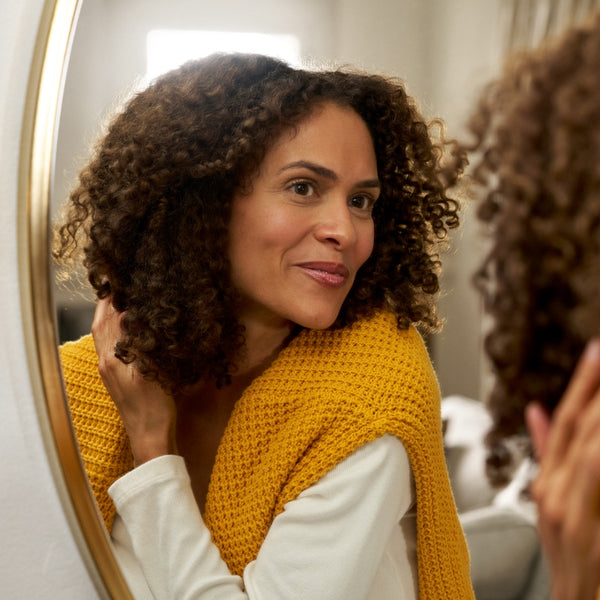 Person with yellow sweater looking at curly hair in mirror