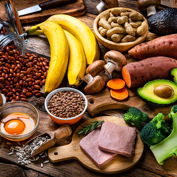 Assorted healthy foods including bananas, nuts, avocados, and meats on a wooden surface.