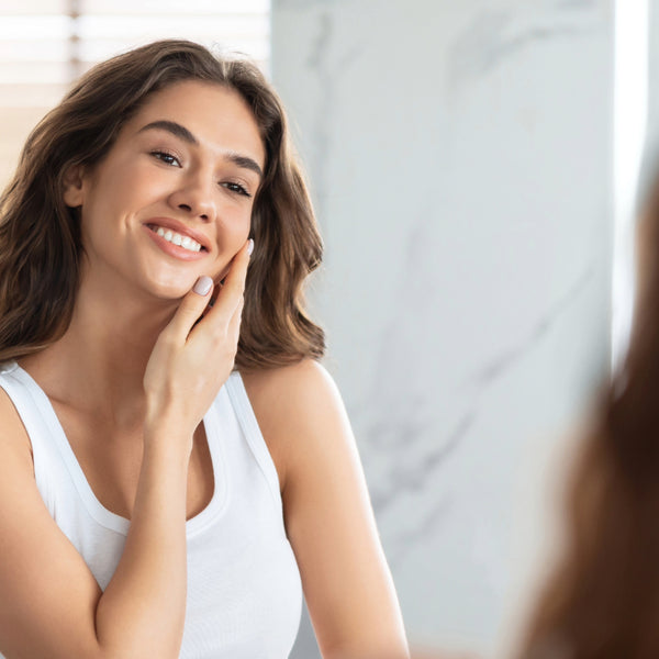 Person in white shirt touching face while looking in bathroom mirror