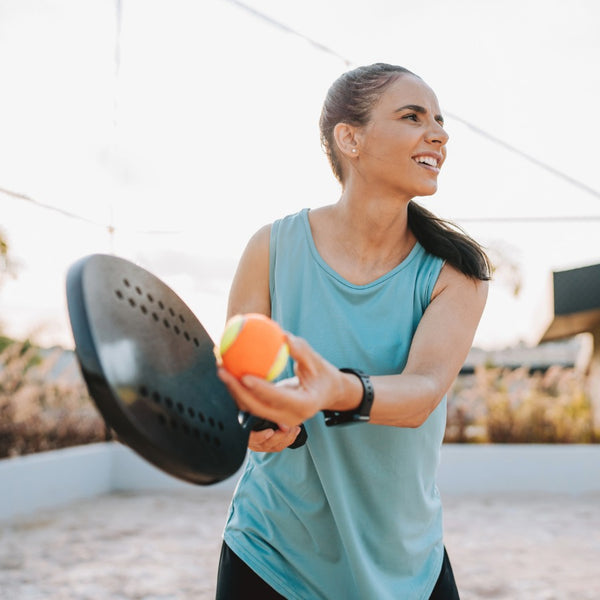 Woman in athletic wear holding a sports ball and a paddle outdoors