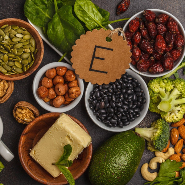 Assorted foods rich in vitamin E on a dark surface with a label showing the letter 'E'.