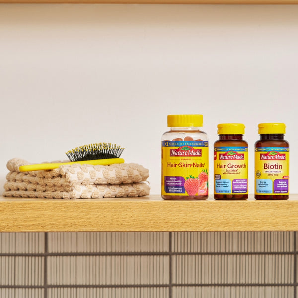 Nature Made hair, skin and nails, Hair Growth & Biotin supplements on a wooden surface next to a hand towel and comb.