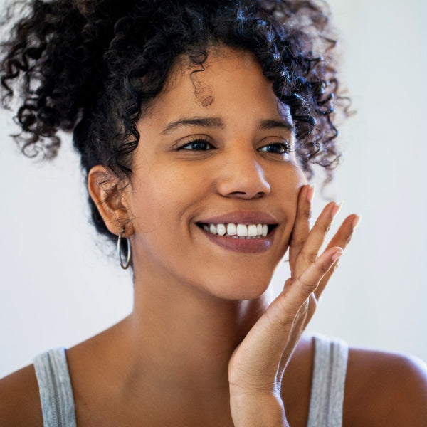 Woman with a bright smile touching her face against a neutral background